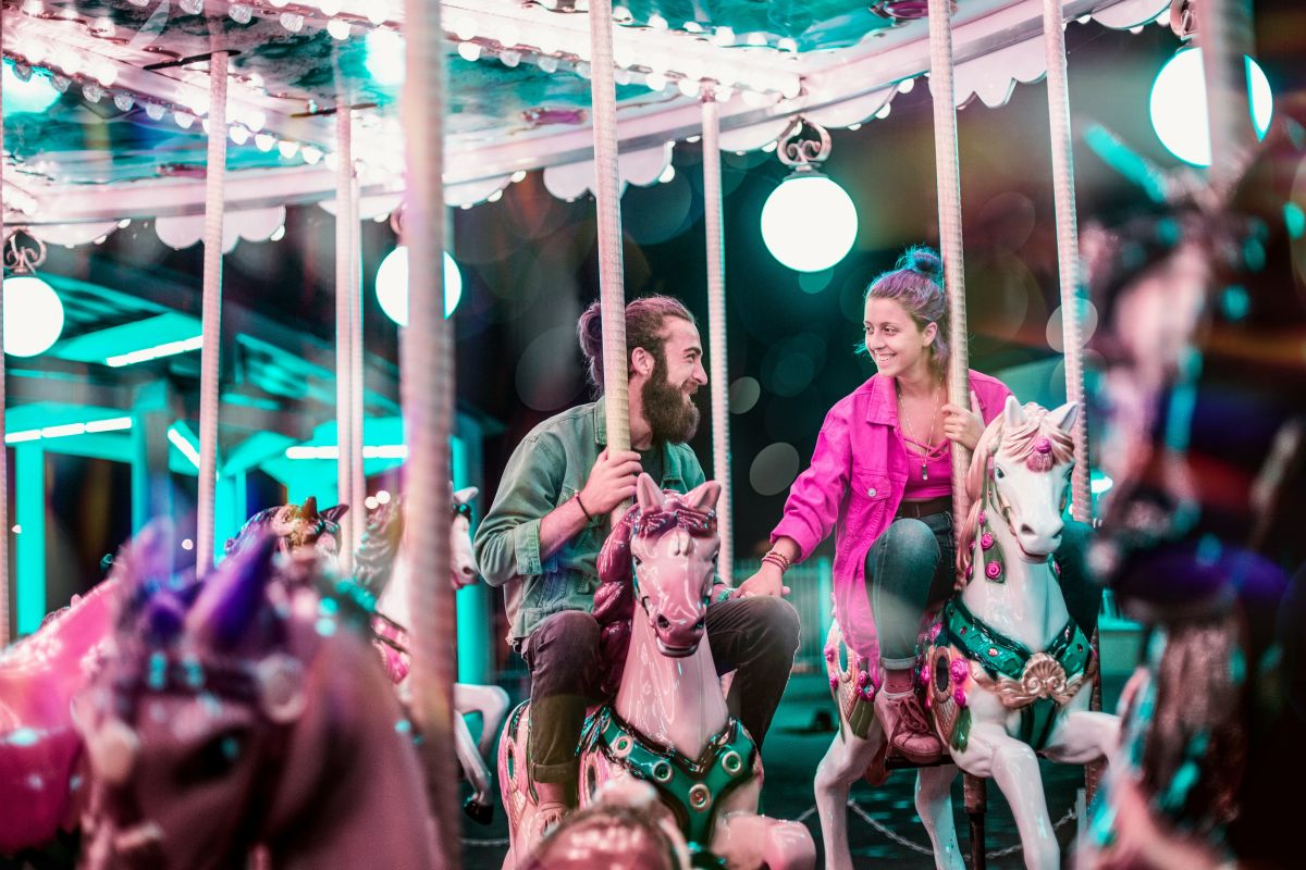 Man and woman riding a merry-go-round after meeting online and smiling at each other